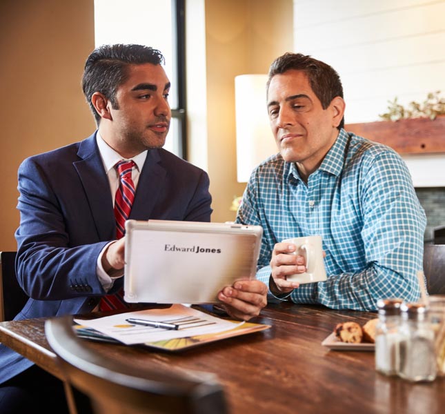 A financial advisor holds a tablet device while having a discussion with a man.