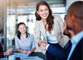 A woman in a business suit shakes the hand of a man.
