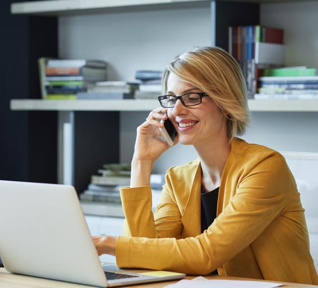 A woman talking on a phone and typing on a laptop