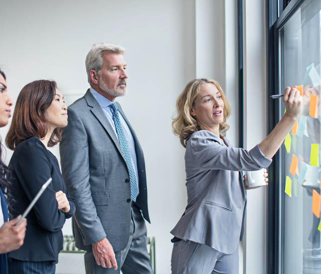 Des professionnels discutent d’idées à écrire sur des papillons adhésifs dans un bureau.