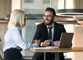 Un homme et une femme assis à une table parlent et regardent un ordinateur portable.
