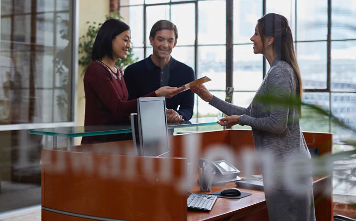Un couple remet des papiers à une femme debout derrière un bureau.