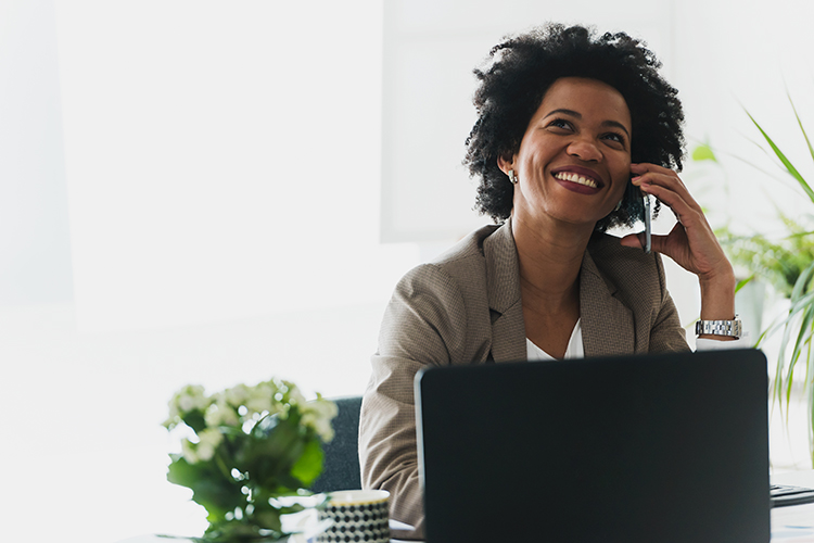 Happy smiling african-american business woman working on laptop at office Women on phone in front of computer